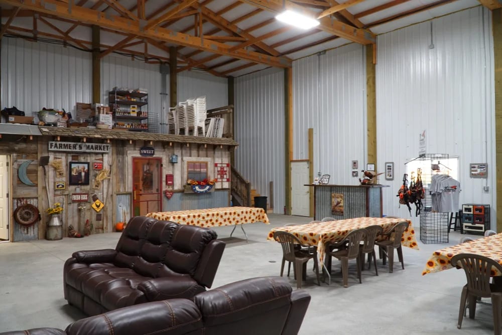 The interior of a large lodge or common area with tables, chairs, and a decorative 'Farmer's Market' facade.