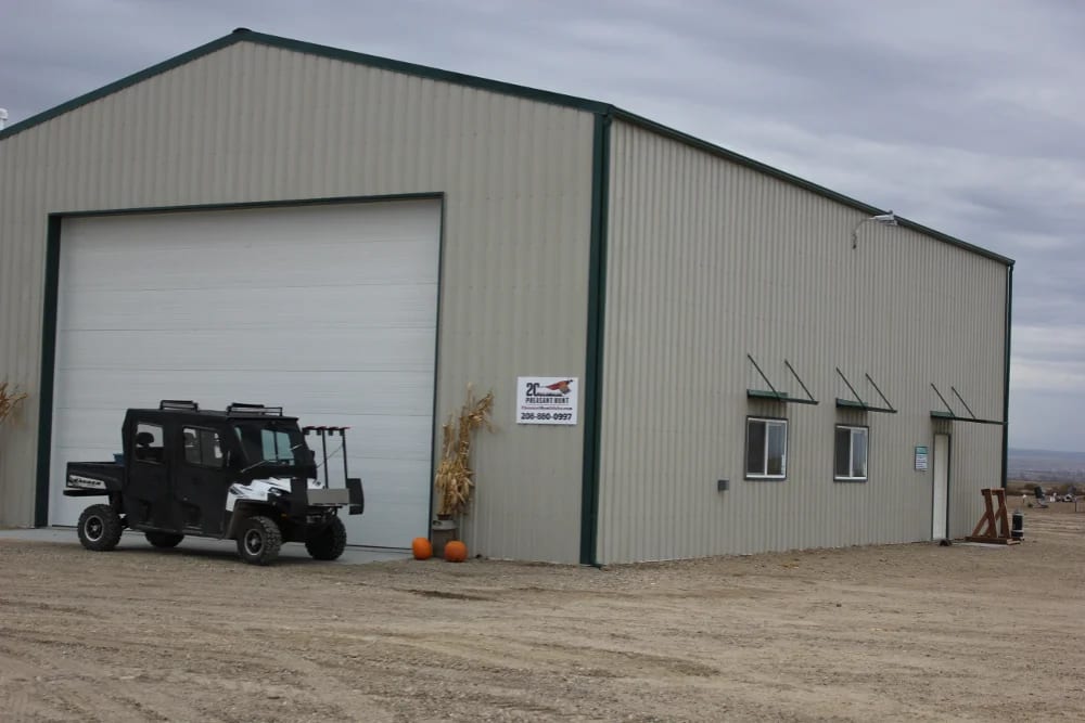 A large metal building with a white garage door and a utility vehicle parked in front.