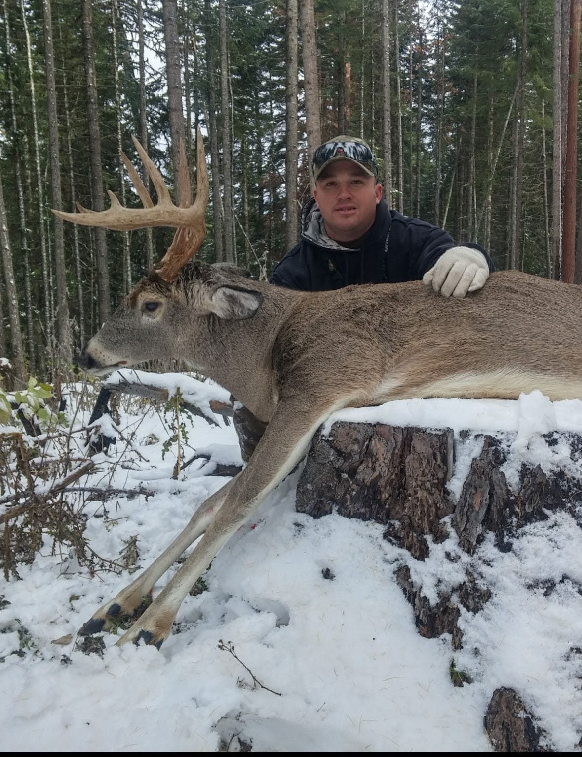 A hunter poses with a harvested whitetail deer in a snowy forest.