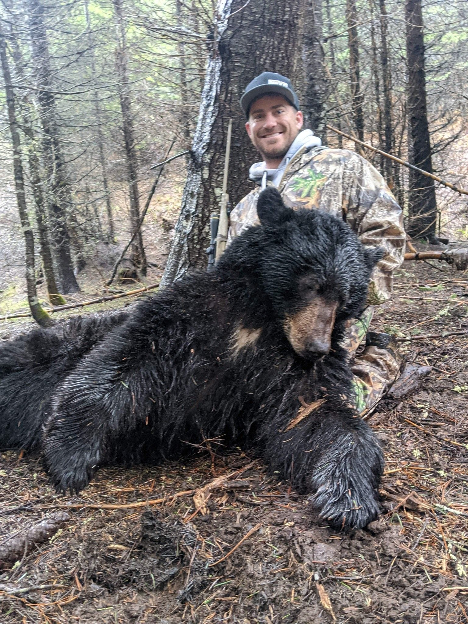 A hunter kneels next to a harvested black bear in a forest.