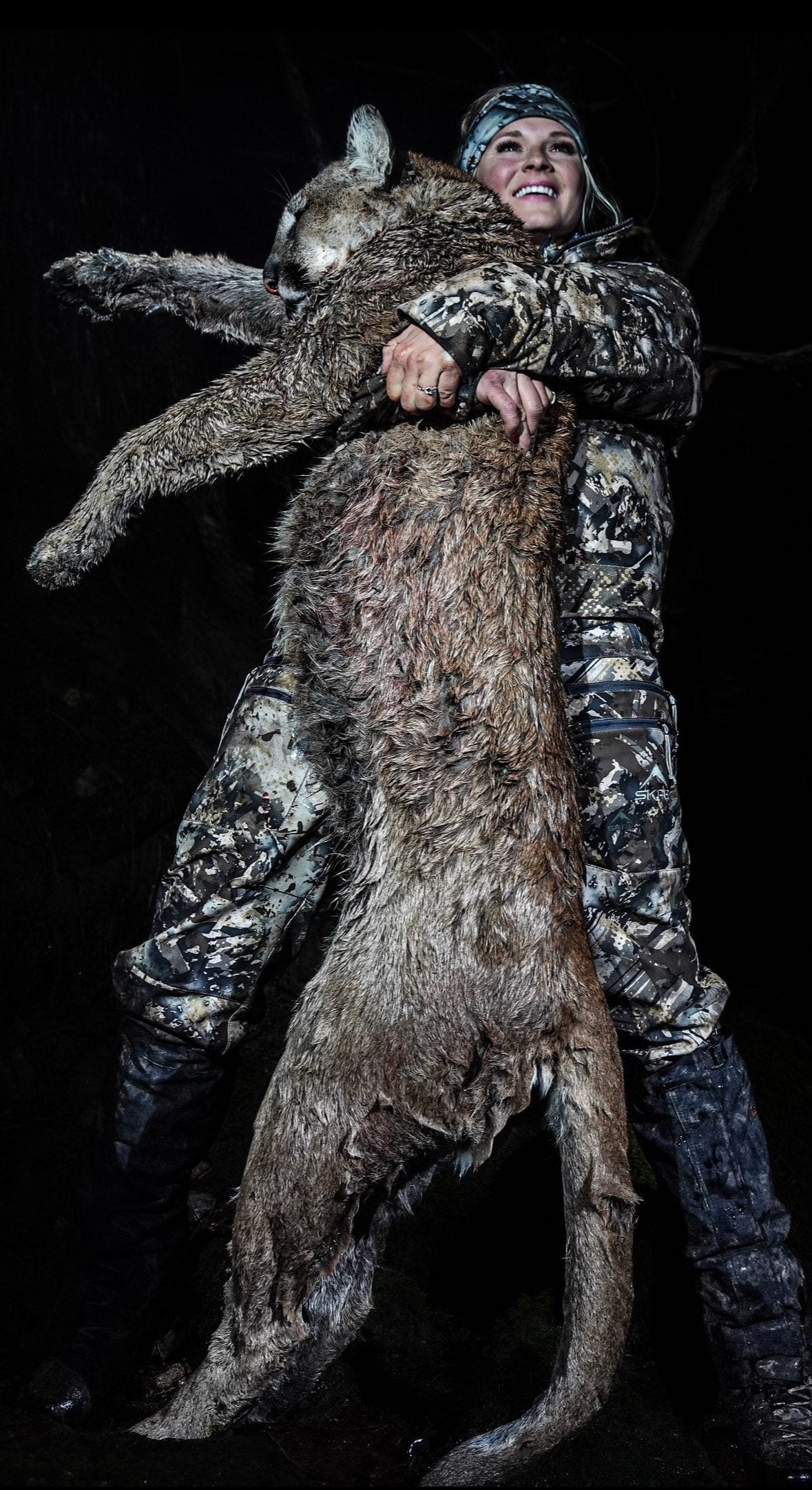 A hunter in camouflage clothing holds a harvested mountain lion.