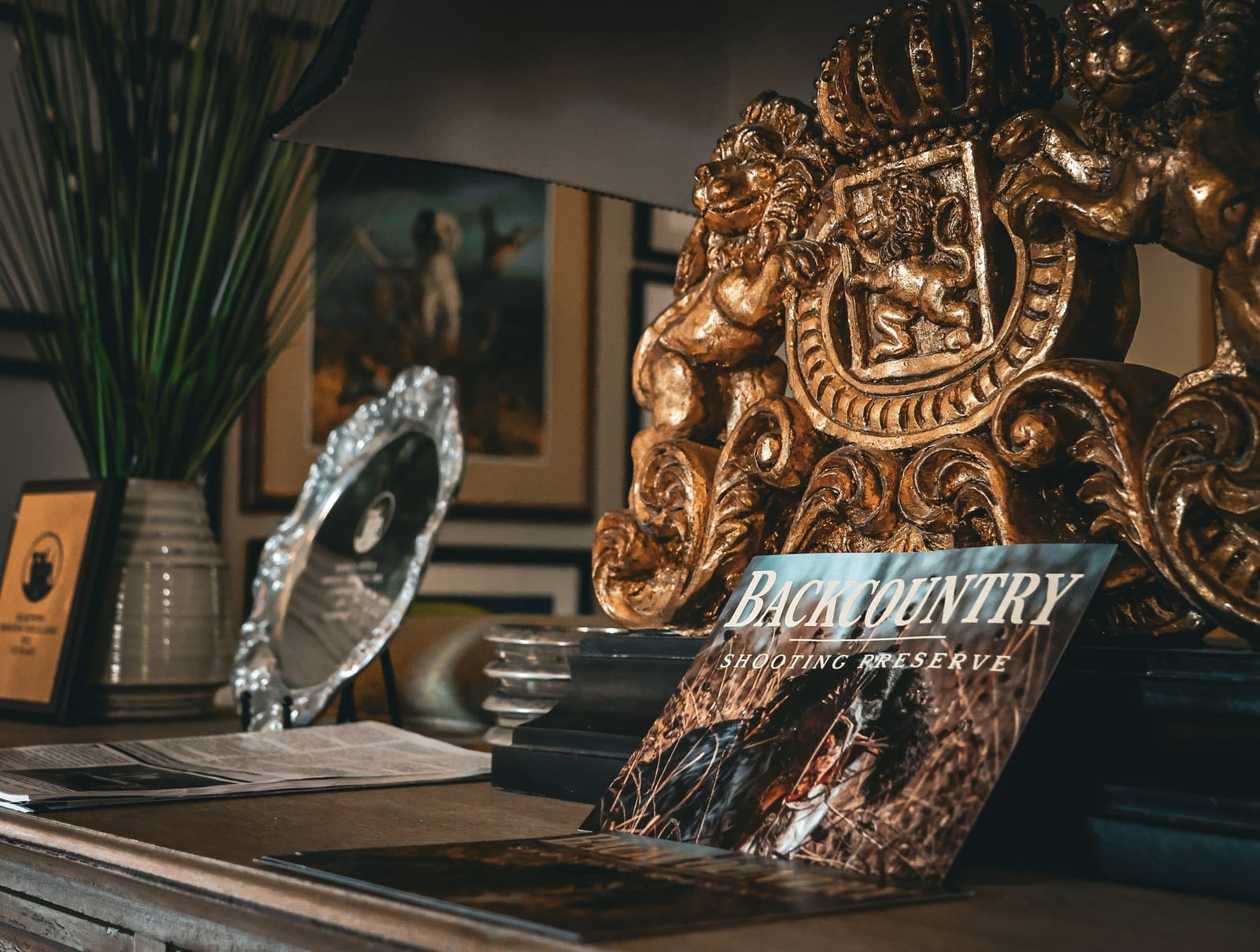 A magazine for Backcountry Shooting Preserve rests on a wooden table next to decorative items and a golden crest.