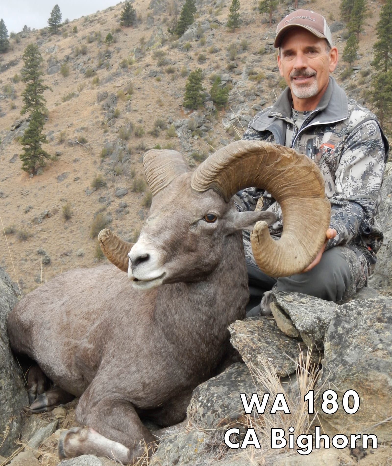 A hunter poses with a harvested bighorn sheep on a rocky hillside.