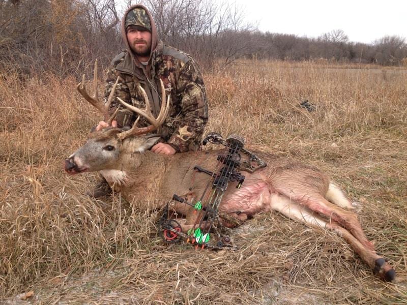 A hunter poses with a harvested whitetail deer in a field.