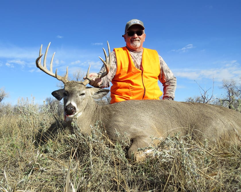 A hunter poses with a harvested whitetail deer in a grassy field.