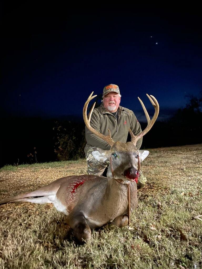 A hunter kneels behind a harvested whitetail deer at night.