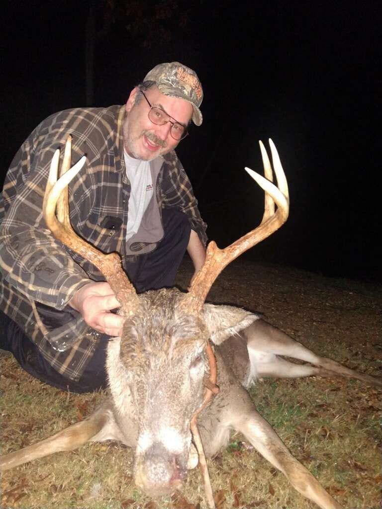 A man kneels next to a harvested whitetail deer at night.