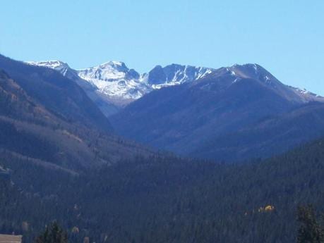 A scenic view of snow-capped mountains and forested valleys under a clear blue sky.
