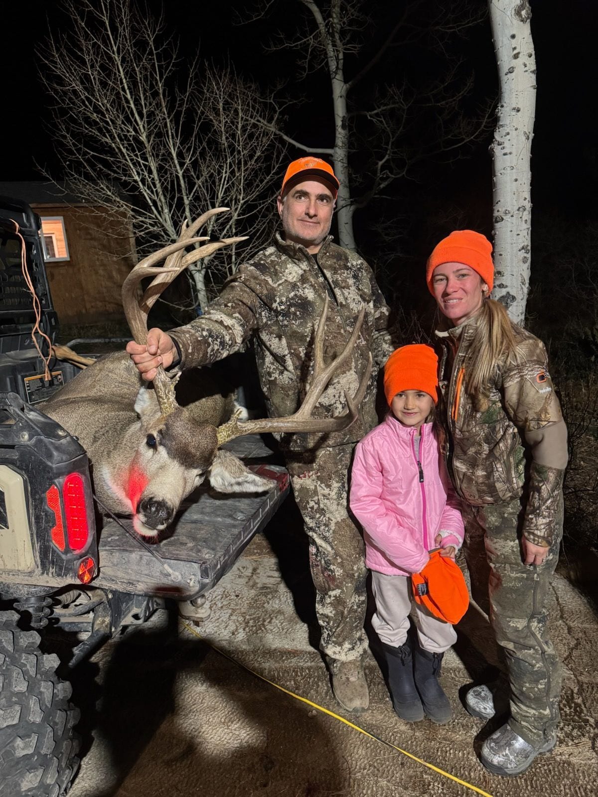 A man, woman, and child pose with a harvested mule deer at night.