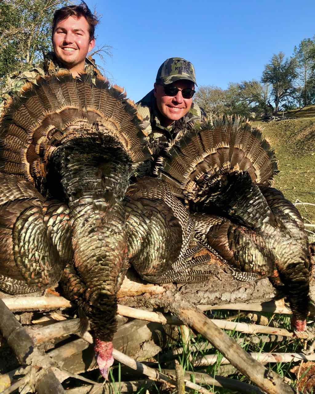 Two hunters pose with two harvested wild turkeys.
