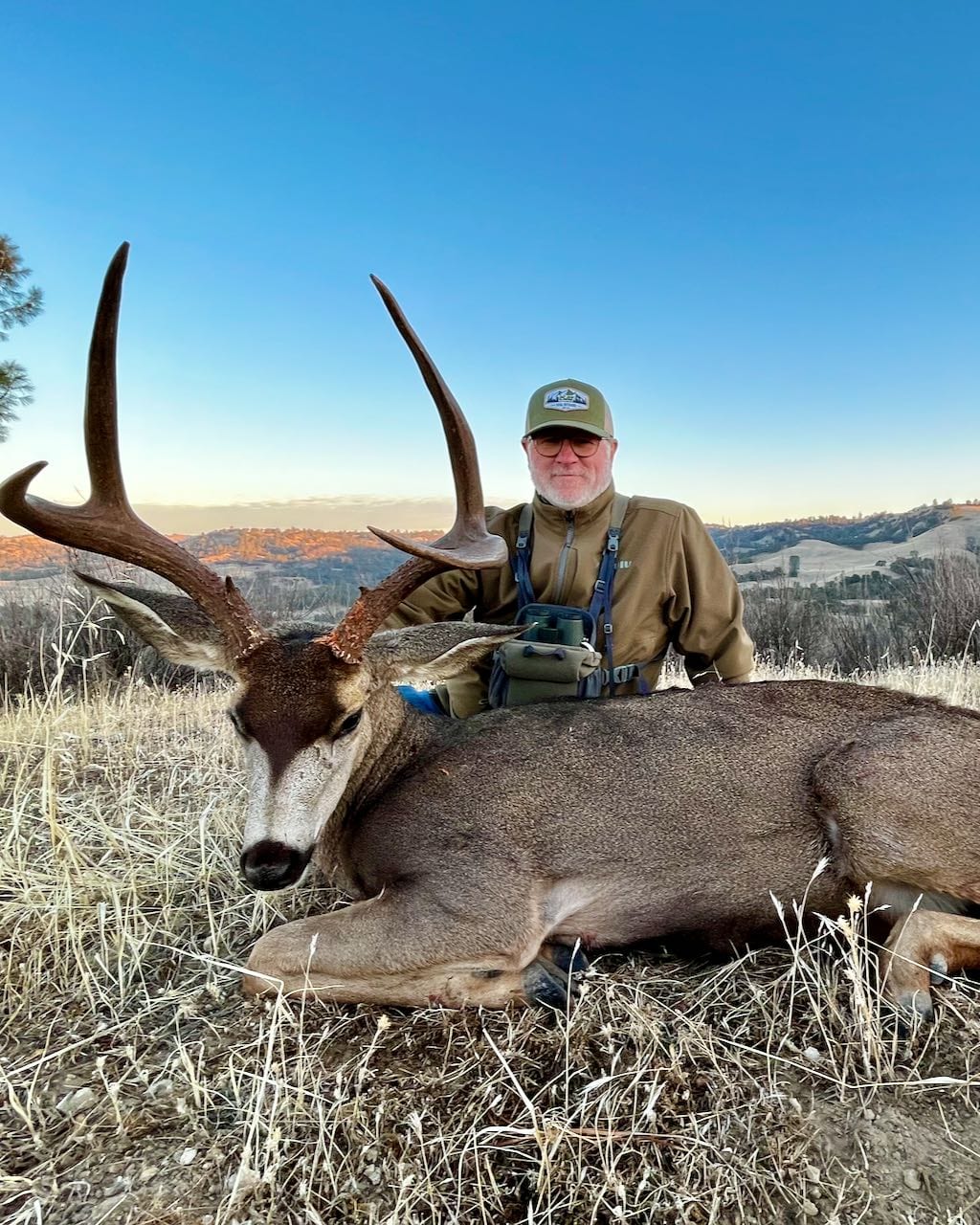A hunter poses with a harvested Columbian blacktail deer in a field.