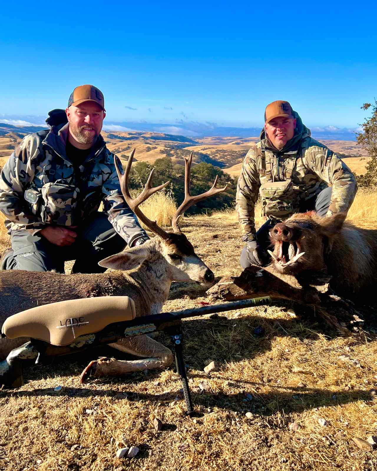 Two hunters pose with a harvested Columbian blacktail deer and a wild boar in a field.