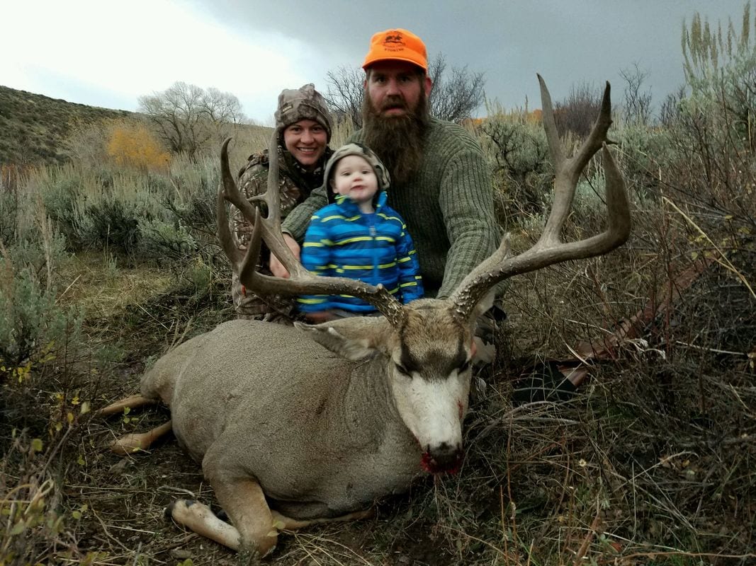 A family poses with a harvested mule deer in a field.