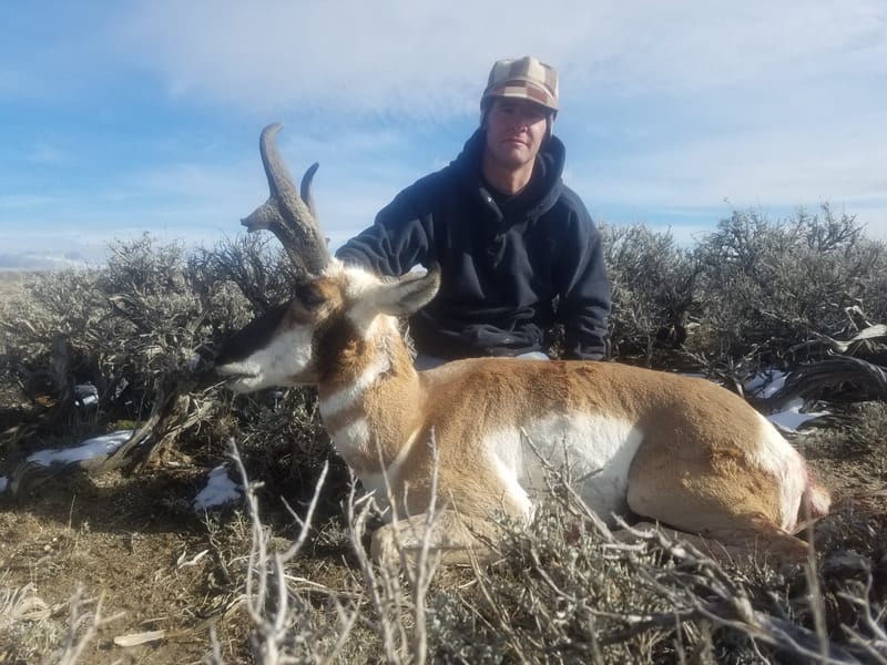 A hunter poses with a harvested pronghorn in a field.