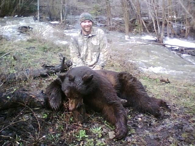 A hunter poses with a harvested black bear next to a stream.
