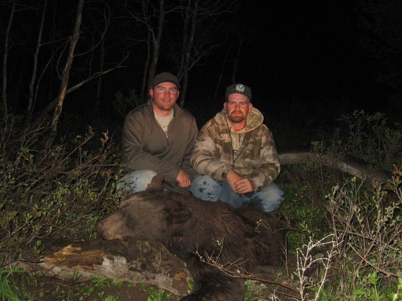 Two hunters pose with a harvested black bear at night.