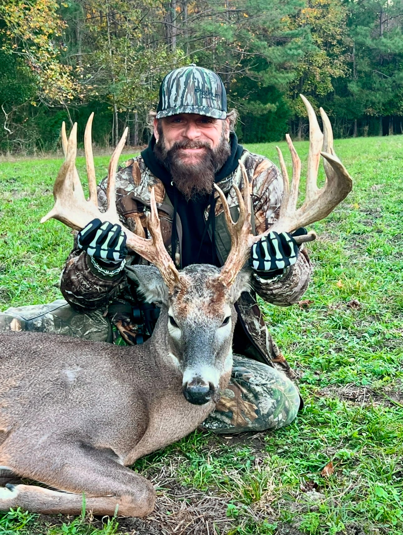 A hunter poses with a harvested whitetail deer in a grassy field.