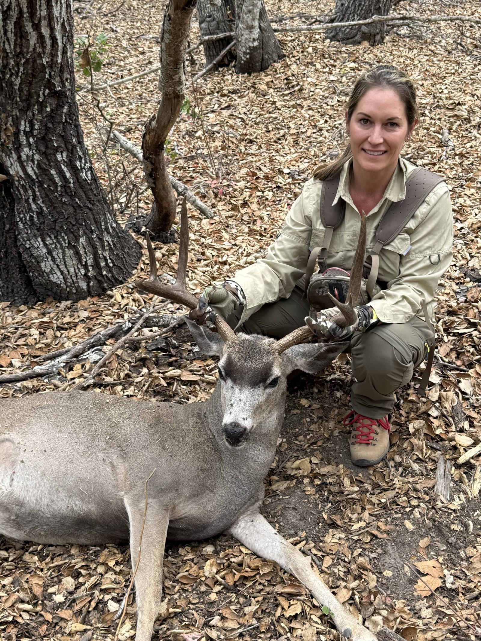 A woman poses with a harvested Columbian blacktail deer in a wooded area.