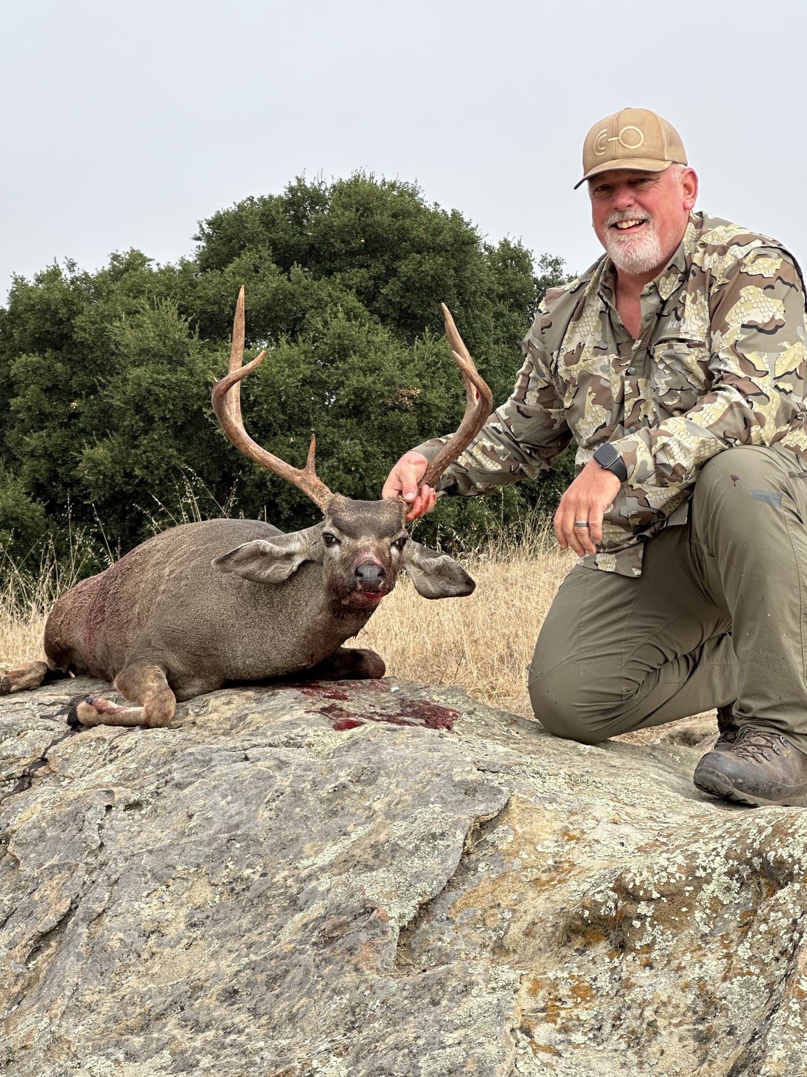 A hunter kneels next to a harvested Columbian blacktail deer on a rock.