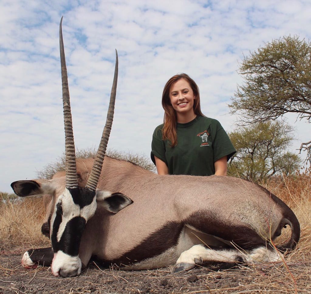 A woman poses with a harvested oryx in a field.