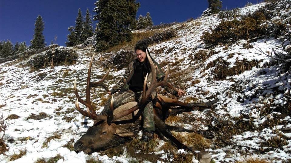 A woman poses with a harvested elk on a snowy hillside.