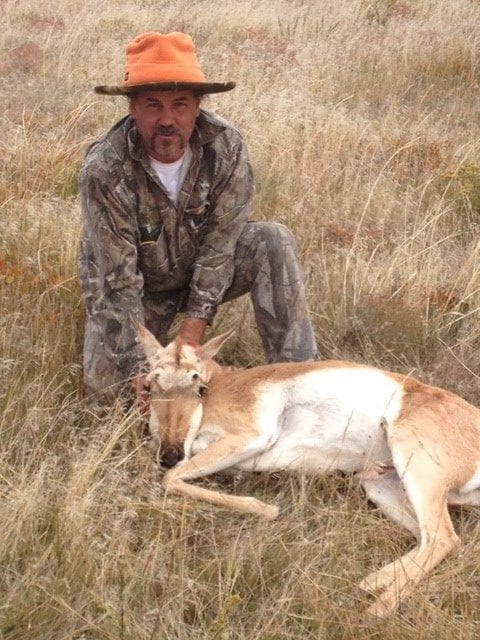 A hunter kneels next to a harvested pronghorn in a grassy field.