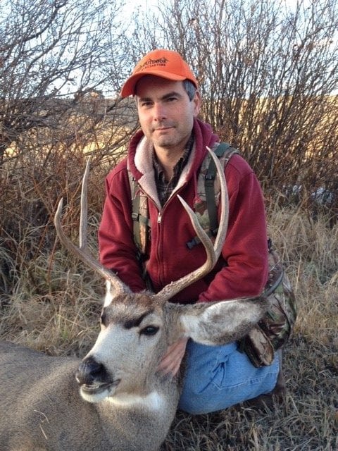 A hunter kneels next to a harvested mule deer.