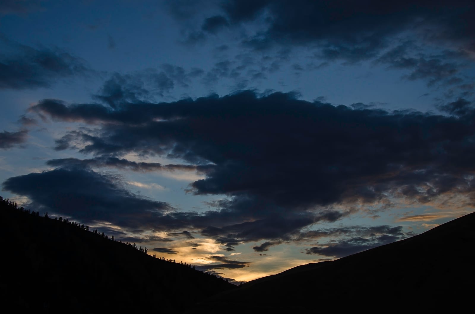 A dramatic sunset or sunrise over mountains with dark clouds in the sky.