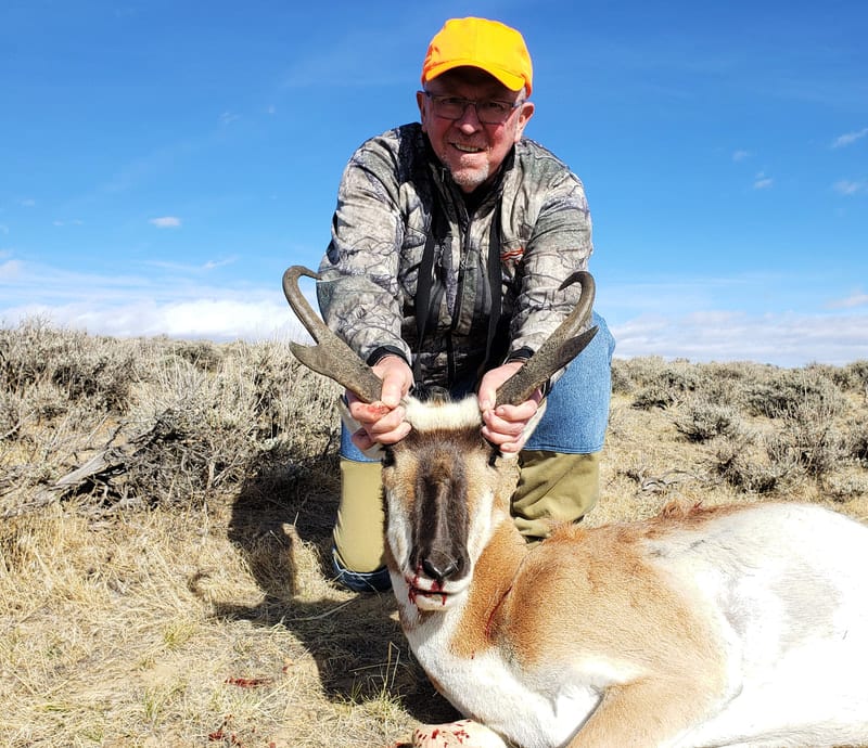 A hunter kneels with a harvested pronghorn in a field.