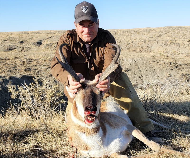 A hunter poses with a harvested pronghorn in a dry, grassy field.