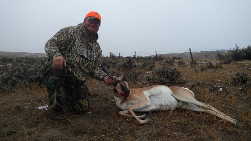 A hunter kneels next to a harvested pronghorn in a field.
