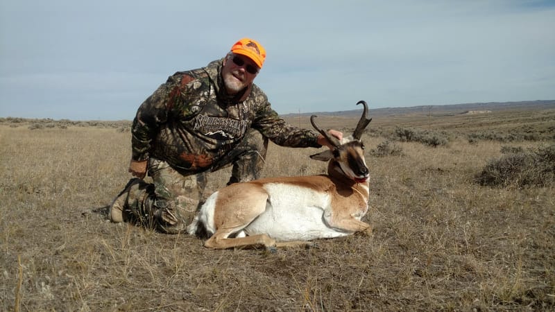 A hunter kneels next to a harvested pronghorn in a field.
