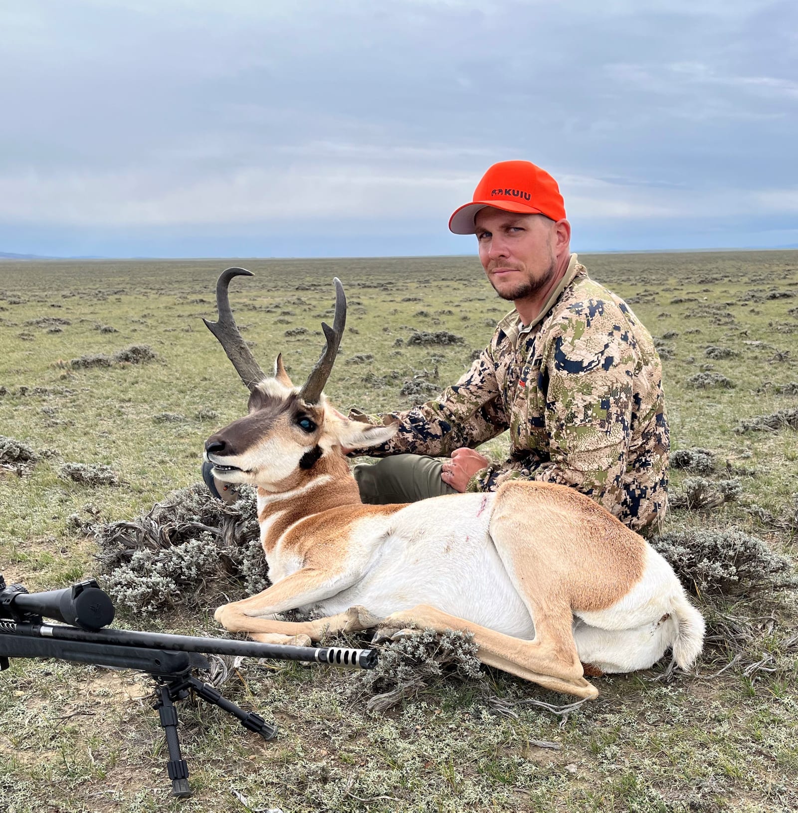 A hunter poses with a harvested pronghorn in a grassy field.