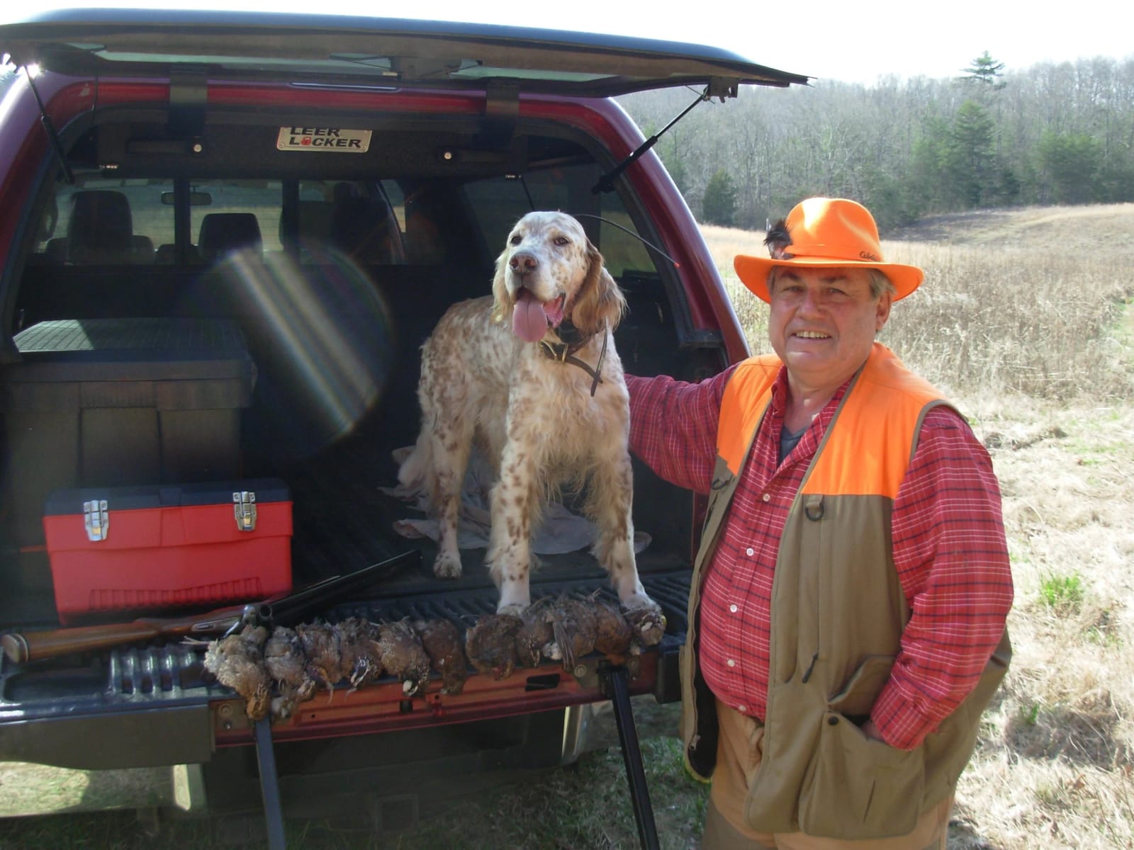 A hunter and his dog pose with harvested northern bobwhite quail in the back of a truck.