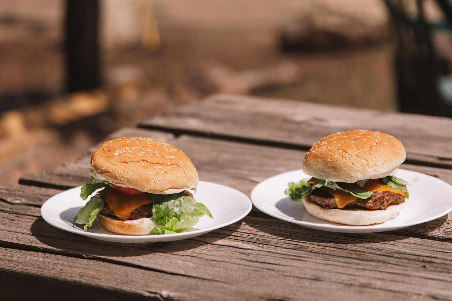 Two hamburgers with cheese and lettuce on white plates on a wooden table.