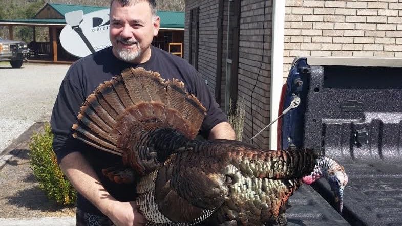 A man holds a harvested wild turkey next to the tailgate of a truck.