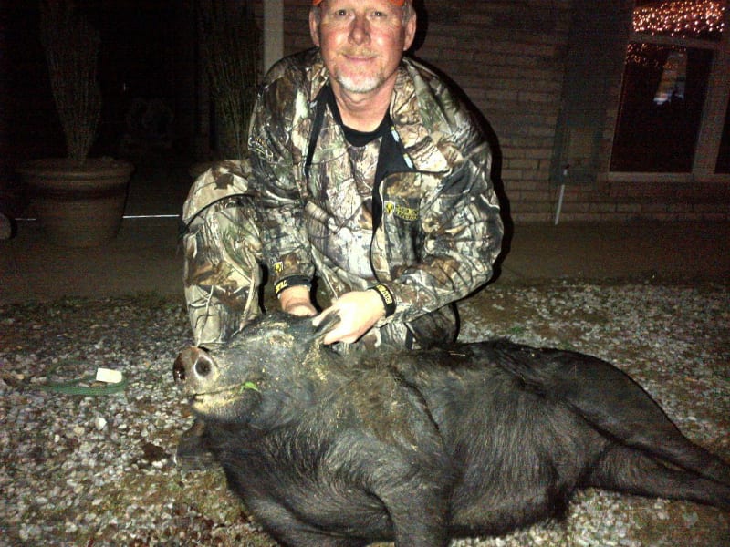 A hunter in camouflage kneels next to a harvested wild boar at night.