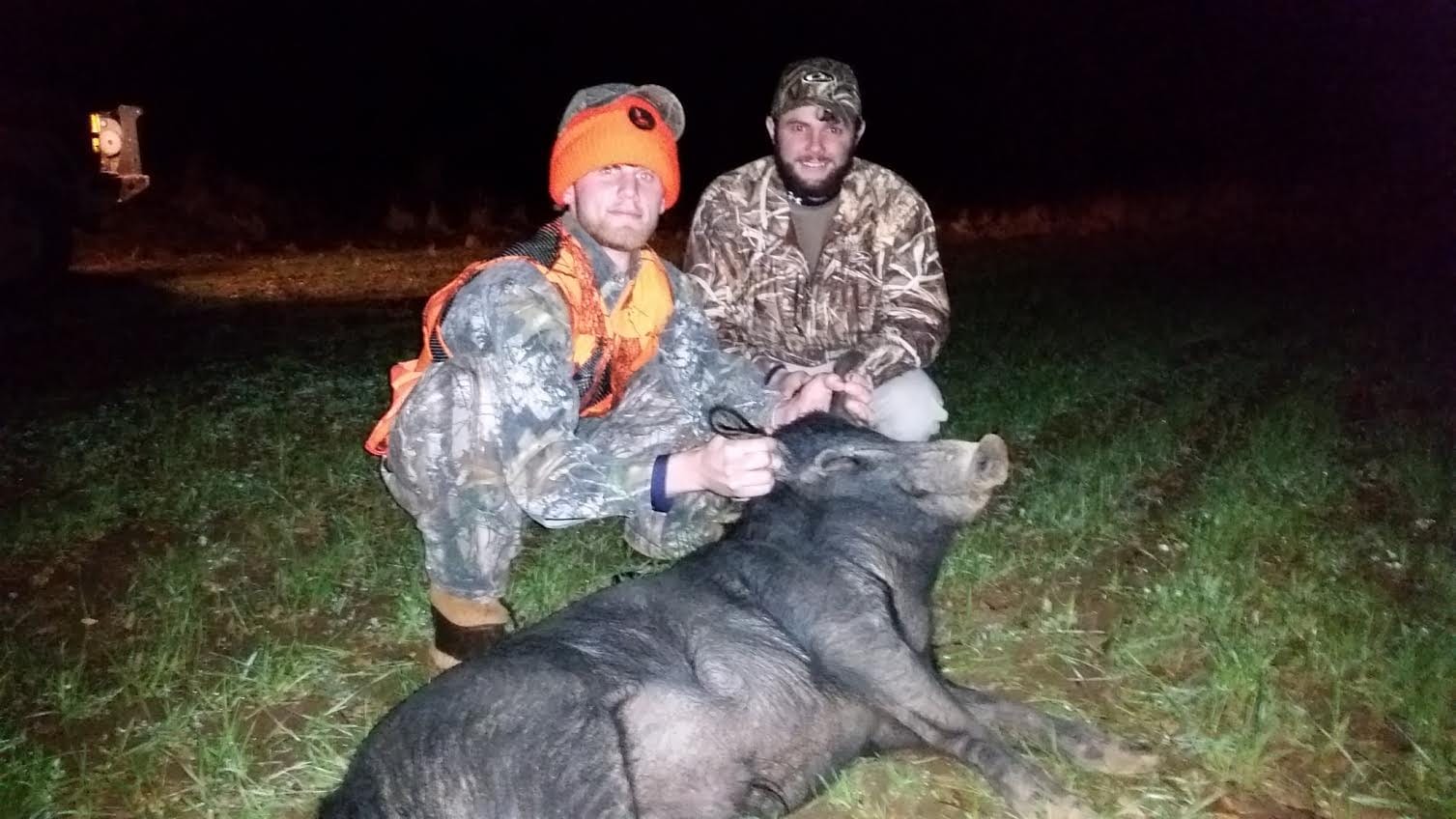 Two hunters pose with a harvested wild boar at night.