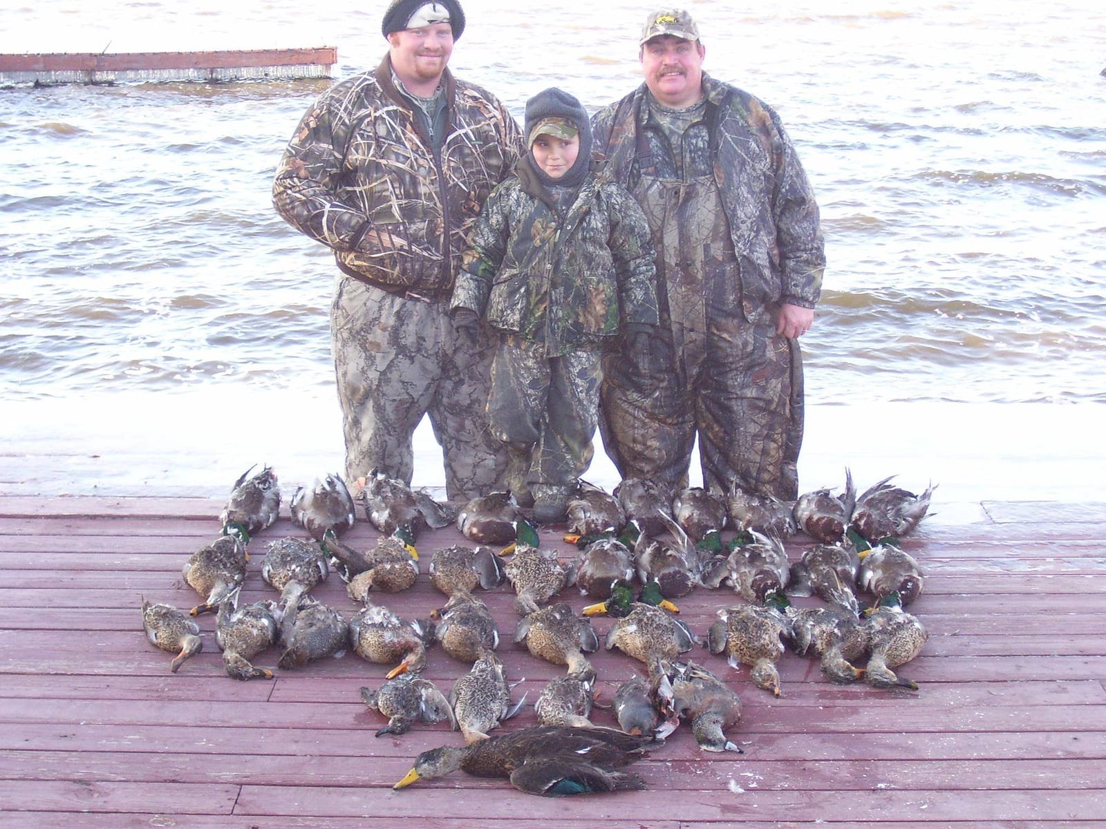 Three hunters pose with their harvest of mallards and black ducks on a dock.