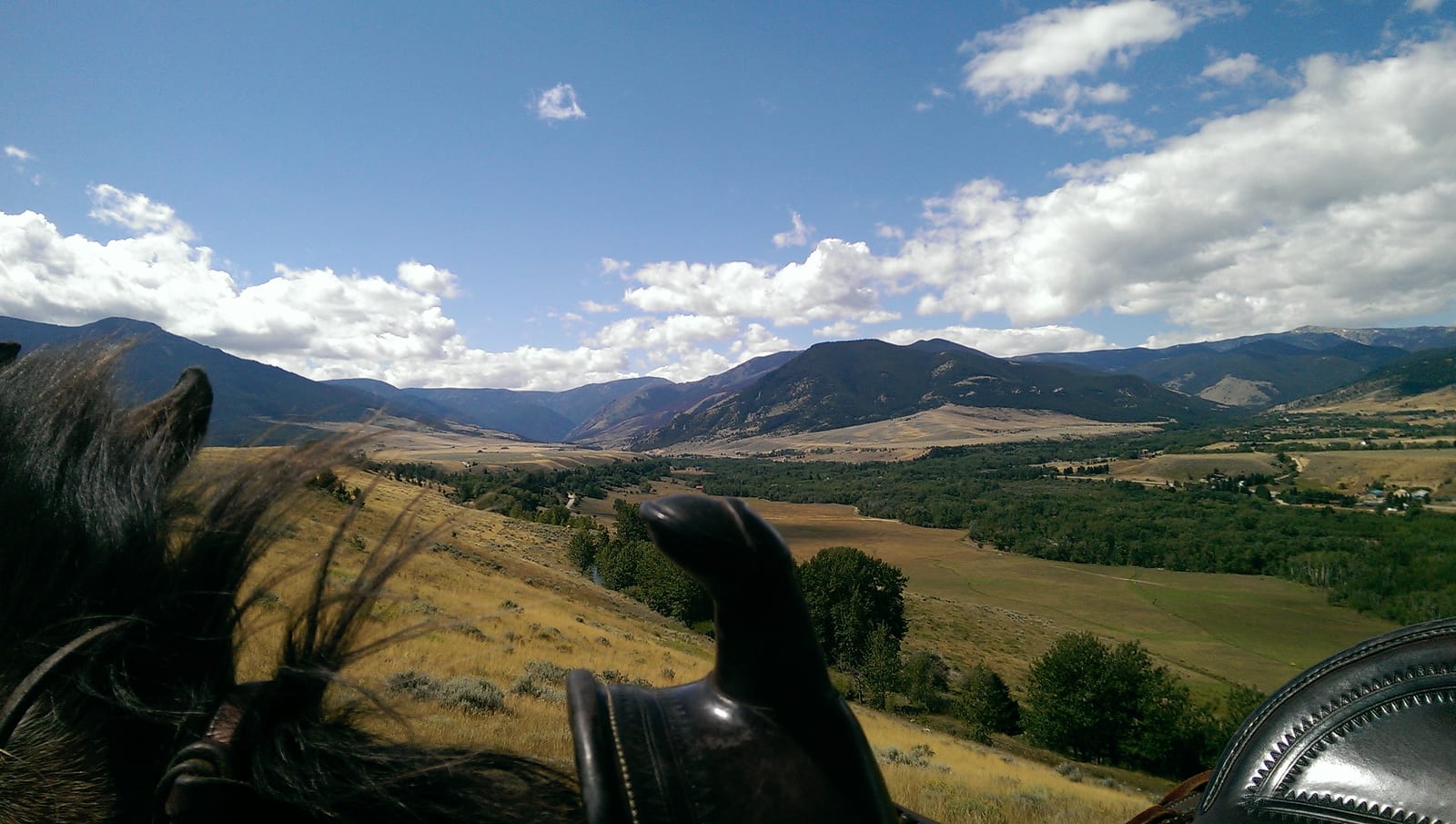 A scenic view of mountains and valleys from horseback under a blue sky.