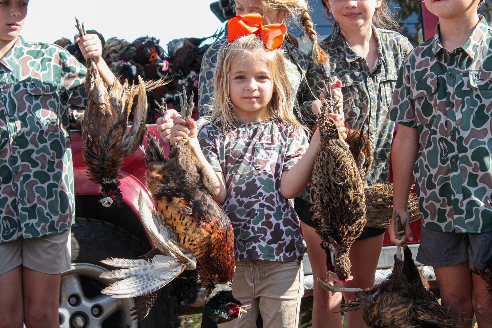 Children in camouflage shirts hold harvested pheasants and quail.