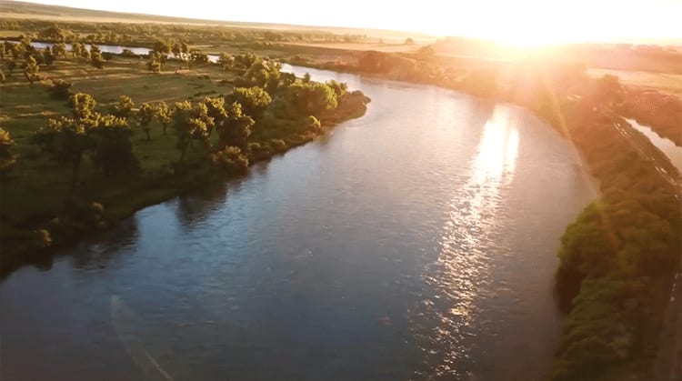 An aerial view of a river winding through a green landscape at sunset.