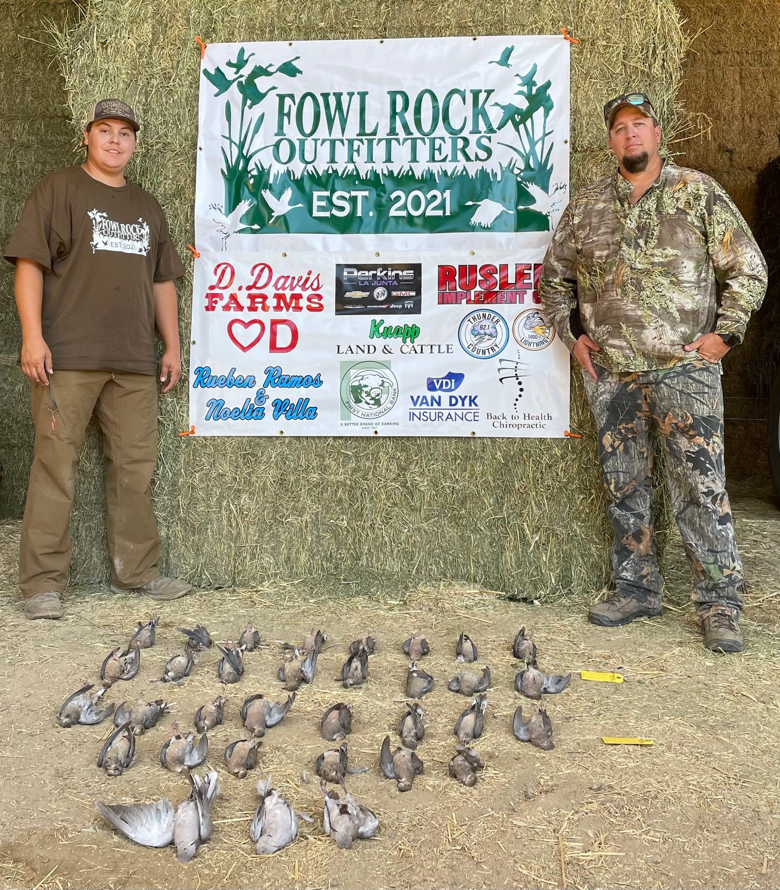 Two hunters pose with a large harvest of mourning doves in front of a Fowl Rock Outfitters banner.