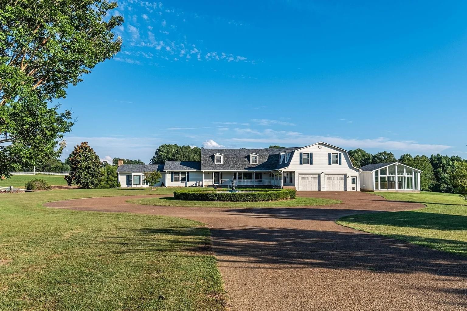 A large white lodge with a circular driveway and green lawn under a blue sky.