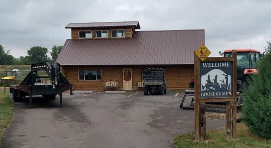 A lodge building with a 'Welcome Goosehump's' sign and vehicles parked outside under a cloudy sky.