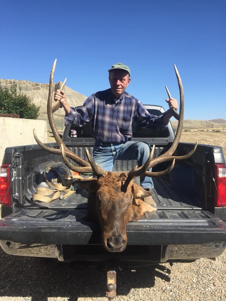 A man poses with a harvested elk head in the back of a pickup truck.