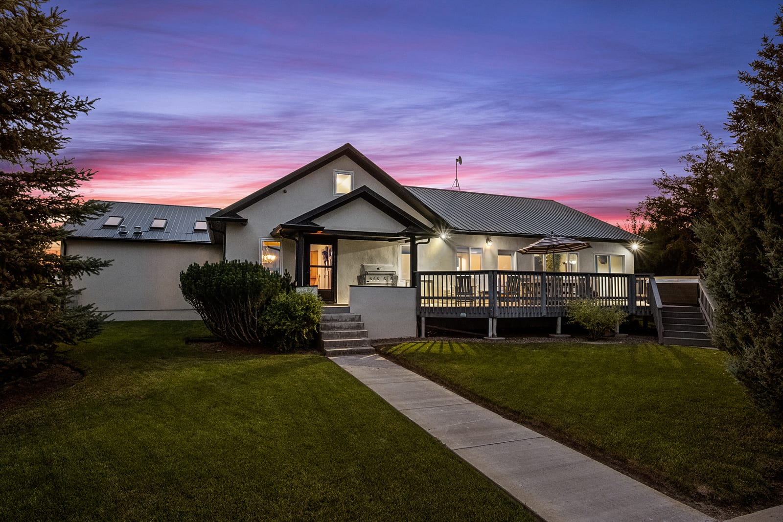 A lodge building with a deck and stairs is illuminated at sunset, with a vibrant sky in the background.