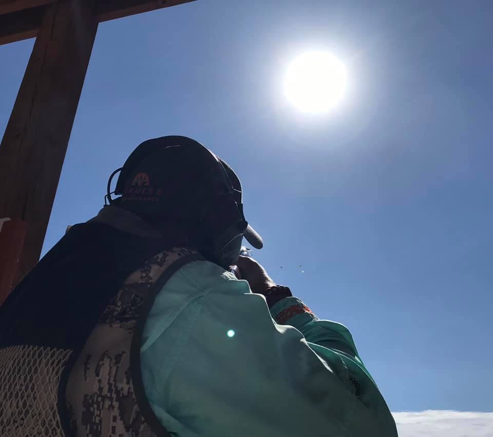 A person wearing ear protection and a cap looks up at the bright sun in a clear blue sky.