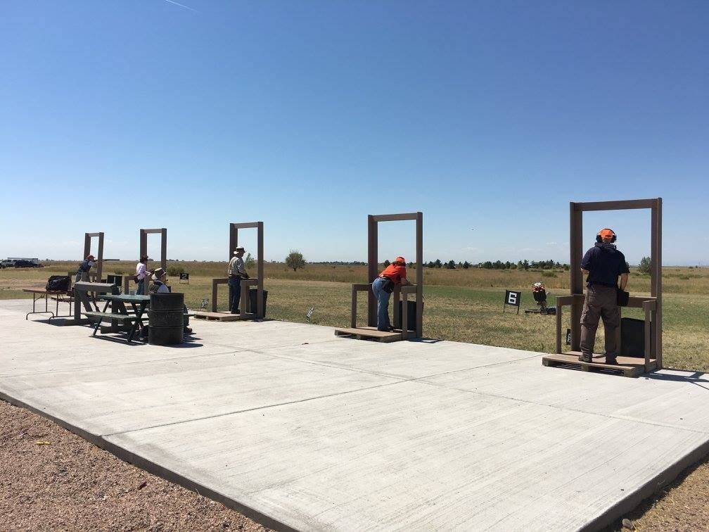People are seen shooting at a range under a clear blue sky.