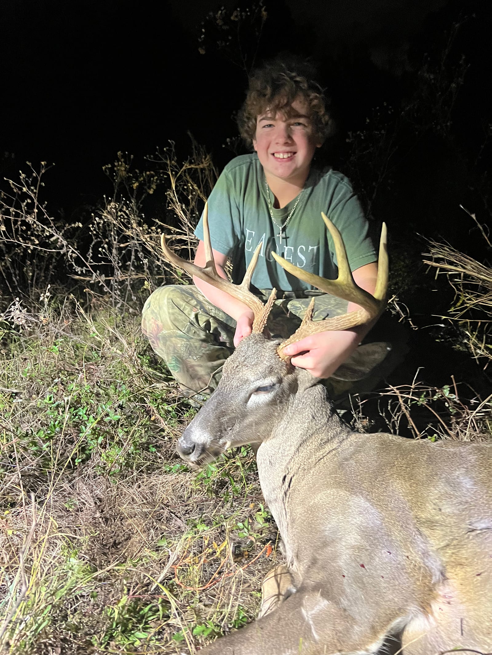 A young hunter poses with a harvested whitetail deer at night.